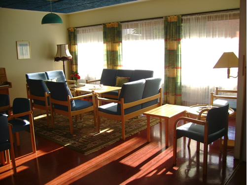 Bilde av en stue møblert med sofaer og stoler med blå puter samt noen trebord